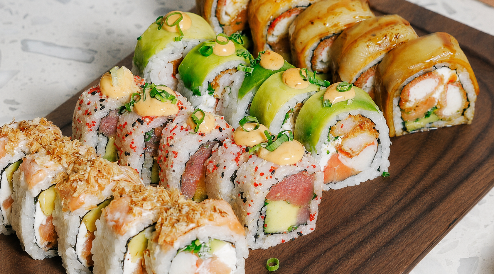 sushi rolls platter vancouver local delicious sushi flavors Best Sushi in Vancouver Colourful uramaki rolls with avocado, sauces, tobiko, and scallions on a wooden board at a Vancouver aburi-style sushi restaurant